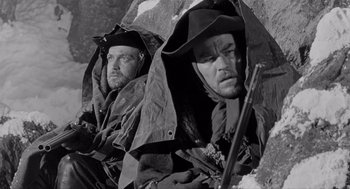 Movie still from “Day of the Outlaw” (1959), directed by André De Toth – A black - and - white photo of two men sitting under an umbrella; Medium shot, Low angle