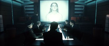 Movie still from “Daybreakers” (2009), directed by Michael Spierig – A group of people sitting at a table in front of a projection screen; Medium shot, Over the shoulder angle
