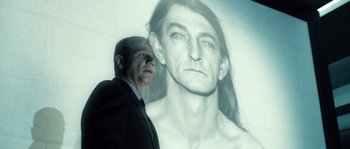 Movie still from “Daybreakers” (2009), directed by Michael Spierig – A man standing next to an image of a man with long hair; Close Up shot, Over the shoulder angle