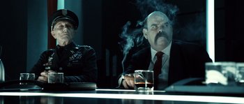Movie still from “Daybreakers” (2009), directed by Michael Spierig – A man smoking a cigarette in front of another man in a suit; Medium shot, Low angle