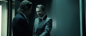 Movie still from “Daybreakers” (2009), directed by Michael Spierig – A man in a suit standing next to another man in a suit; Medium shot, Over the shoulder angle