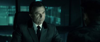 Movie still from “Daybreakers” (2009), directed by Michael Spierig – A man wearing a suit and tie in front of a computer screen; Close Up shot, Over the shoulder angle