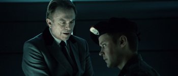 Movie still from “Daybreakers” (2009), directed by Michael Spierig – Two men in suits talking to each other in a dark room; Close Up shot, Over the shoulder angle