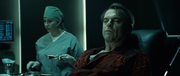 Movie still from “Daybreakers” (2009), directed by Michael Spierig – A man in a red shirt is sitting in a chair; Close Up shot, Over the shoulder angle