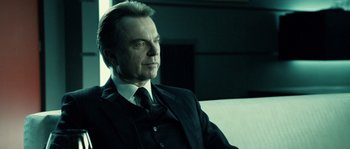 Movie still from “Daybreakers” (2009), directed by Michael Spierig – A man in a suit and tie sitting on a couch; Close Up shot, Over the shoulder angle