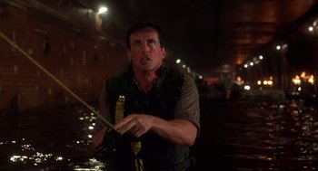 Movie still from “Daylight” (1996), directed by Rob Cohen – A man holding a fishing pole in a flooded area at night; Medium shot, Low angle