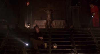 Movie still from “Daylight” (1996), directed by Rob Cohen – A man sitting on some steps in front of a crucifixion; Wide shot, Low angle