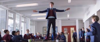 Movie still from “The Kid Who Would Be King” (2019), directed by Joe Cornish – A man standing on top of a table in front of a group of people; Wide shot, Low angle