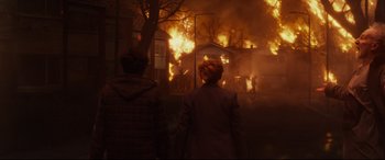 Movie still from “The Kid Who Would Be King” (2019), directed by Joe Cornish – Two people standing in front of a burning house; Wide shot, Over the shoulder angle