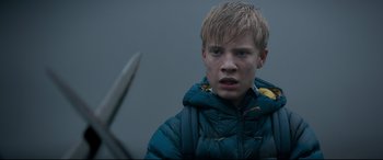 Movie still from “The Kid Who Would Be King” (2019), directed by Joe Cornish – A young man in a blue jacket with a knife in his hand; Close Up shot, Over the shoulder angle