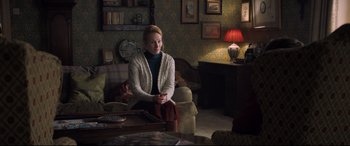Movie still from “The Kid Who Would Be King” (2019), directed by Joe Cornish – A woman sitting on a couch in a living room; Medium shot, Over the shoulder angle