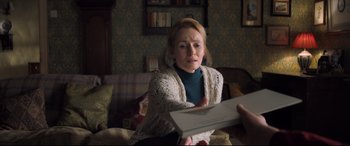 Movie still from “The Kid Who Would Be King” (2019), directed by Joe Cornish – A woman sitting on a couch holding an open book; Close Up shot, Over the shoulder angle