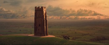Movie still from “The Kid Who Would Be King” (2019), directed by Joe Cornish – A horse drawn carriage traveling past a tower in a field; Extreme Wide shot, High angle