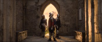 Movie still from “The Kid Who Would Be King” (2019), directed by Joe Cornish – A group of men in medieval garb standing in front of an archway; Wide shot, Low angle