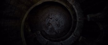 Movie still from “The Kid Who Would Be King” (2019), directed by Joe Cornish – A group of people sitting in a circle in a dark room; Extreme Wide shot, Overhead angle