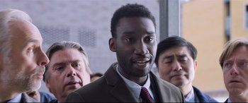Movie still from “The Kid Who Would Be King” (2019), directed by Joe Cornish – A man in a brown suit and a red tie; Close Up shot, Over the shoulder angle