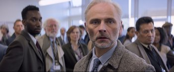 Movie still from “The Kid Who Would Be King” (2019), directed by Joe Cornish – A man with a beard and a tie in front of a group of people; Close Up shot, Over the shoulder angle
