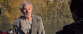 Movie still from “The Kid Who Would Be King” (2019), directed by Joe Cornish – An older man standing next to a body of water; Medium shot, Over the shoulder angle