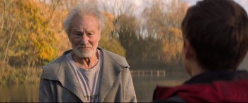 Movie still from “The Kid Who Would Be King” (2019), directed by Joe Cornish – An old man with a gray beard is standing by the water; Close Up shot, Over the shoulder angle