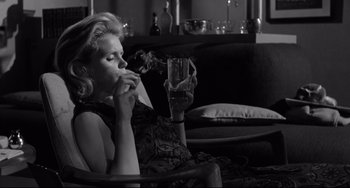 Movie still from “Days of Wine and Roses” (1962), directed by Blake Edwards – A black and white photo of a woman smoking a cigarette and drinking a glass of water; Medium shot, Low angle