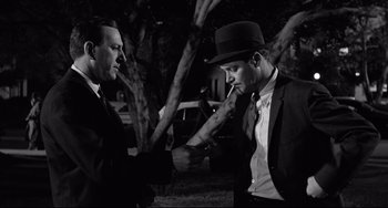Movie still from “Days of Wine and Roses” (1962), directed by Blake Edwards – A man in a suit and a man in a hat are talking to each other; Medium shot, Over the shoulder angle