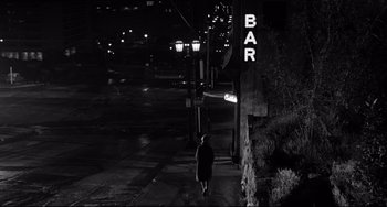 Movie still from “Days of Wine and Roses” (1962), directed by Blake Edwards – A person walking down a street at night; Extreme Wide shot, Over the shoulder angle