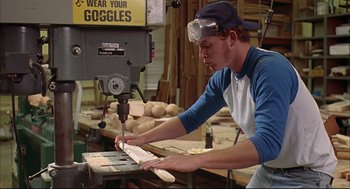 Movie still from “Dazed and Confused” (1993), directed by Richard Linklater – A man using a drill to make a wooden object; Medium shot, Low angle