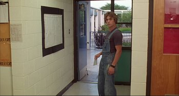 Movie still from “Dazed and Confused” (1993), directed by Richard Linklater – A young man in overalls standing in front of a door; Medium shot, Over the shoulder angle
