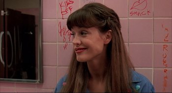 Movie still from “Dazed and Confused” (1993), directed by Richard Linklater – A woman with long brown hair and bangs smiles for the camera; Close Up shot, Over the shoulder angle