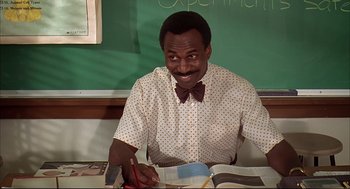 Movie still from “Dazed and Confused” (1993), directed by Richard Linklater – A man sitting at a table with a book and pen; Medium shot, Low angle
