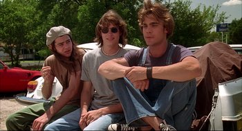 Movie still from “Dazed and Confused” (1993), directed by Richard Linklater – A group of young men sitting next to each other on the ground; Medium shot, Low angle