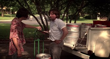 Movie still from “Dazed and Confused” (1993), directed by Richard Linklater – A man standing next to a man holding a clipboard; Medium shot, Over the shoulder angle