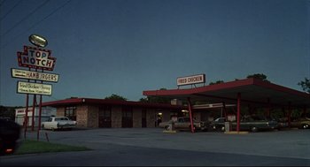 Movie still from “Dazed and Confused” (1993), directed by Richard Linklater – A drive - thru restaurant with a car parked in front of it; Extreme Wide shot, Low angle