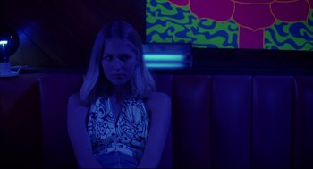 Movie still from “Dazed and Confused” (1993), directed by Richard Linklater – A woman sitting on a bench in a room lit up with neon lights; Medium shot, Low angle