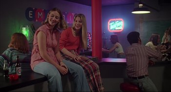 Movie still from “Dazed and Confused” (1993), directed by Richard Linklater – Two young women sitting on a bench in a room with neon lights; Medium shot, Low angle