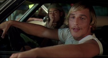 Movie still from “Dazed and Confused” (1993), directed by Richard Linklater – A man driving a car while another man sits in the passenger's seat; Close Up shot, Low angle