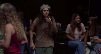 Movie still from “Dazed and Confused” (1993), directed by Richard Linklater – A man with long black hair and a hat smoking a cigarette in front of a crowd; Medium shot, Low angle