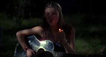Movie still from “Dazed and Confused” (1993), directed by Richard Linklater – A woman sitting on a guitar with a lit cigarette in her mouth; Medium shot, Over the shoulder angle