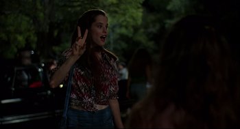 Movie still from “Dazed and Confused” (1993), directed by Richard Linklater – A woman with her hand up in a peace sign; Medium shot, Over the shoulder angle