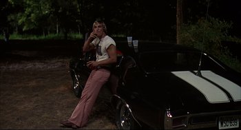 Movie still from “Dazed and Confused” (1993), directed by Richard Linklater – A man sitting on the hood of a black car; Medium shot, Low angle