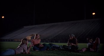 Movie still from “Dazed and Confused” (1993), directed by Richard Linklater – A group of people sitting on top of a grass covered field; Wide shot, High angle
