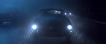 Movie still from “Dead Calm” (1989), directed by Phillip Noyce – A car driving down a street at night with headlights on; Wide shot, High angle