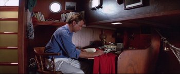 Movie still from “Dead Calm” (1989), directed by Phillip Noyce – A man sitting at a table looking at a book; Medium shot, High angle
