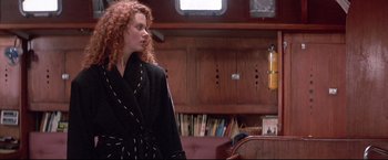 Movie still from “Dead Calm” (1989), directed by Phillip Noyce – A woman with red curly hair standing in a living room; Medium shot, Over the shoulder angle