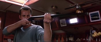 Movie still from “Dead Calm” (1989), directed by Phillip Noyce – A man holding a baseball bat in a room; Medium shot, Low angle