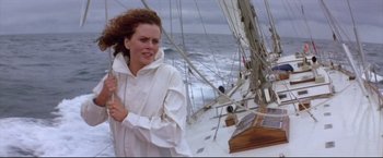 Movie still from “Dead Calm” (1989), directed by Phillip Noyce – A woman in a white jacket standing on a sailboat in the ocean; Medium shot, Low angle