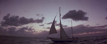 Movie still from “Dead Calm” (1989), directed by Phillip Noyce – A sailboat in the ocean under a cloudy sky at dusk; Extreme Wide shot, Low angle