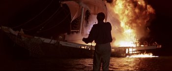Movie still from “Dead Calm” (1989), directed by Phillip Noyce – A man standing in front of a burning boat; Wide shot, Low angle