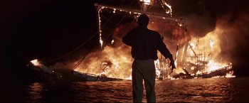 Movie still from “Dead Calm” (1989), directed by Phillip Noyce – A man standing in front of a boat on fire at night; Wide shot, Low angle