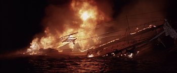Movie still from “Dead Calm” (1989), directed by Phillip Noyce – A large fire is burning in the dark sky; Extreme Wide shot, Low angle